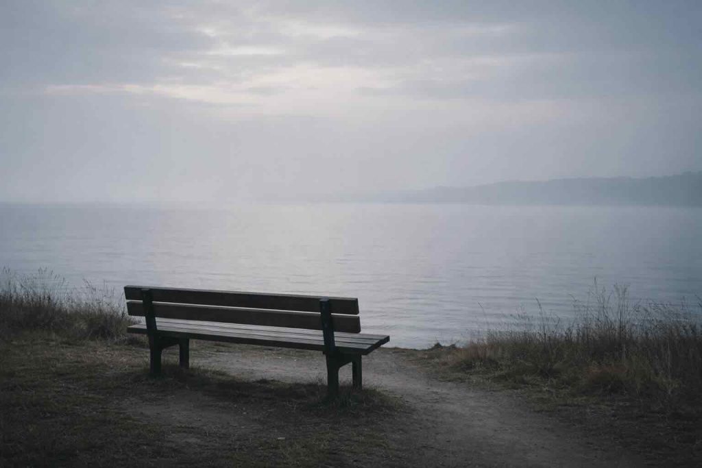 Stille tåget kystlandskab med tom bænk vendt mod rolig horisont som symbol på depression